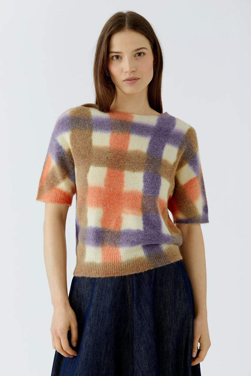 Frau im karierten Pullover in Orange, Lila und Beige, kombiniert mit einem blauen Rock.