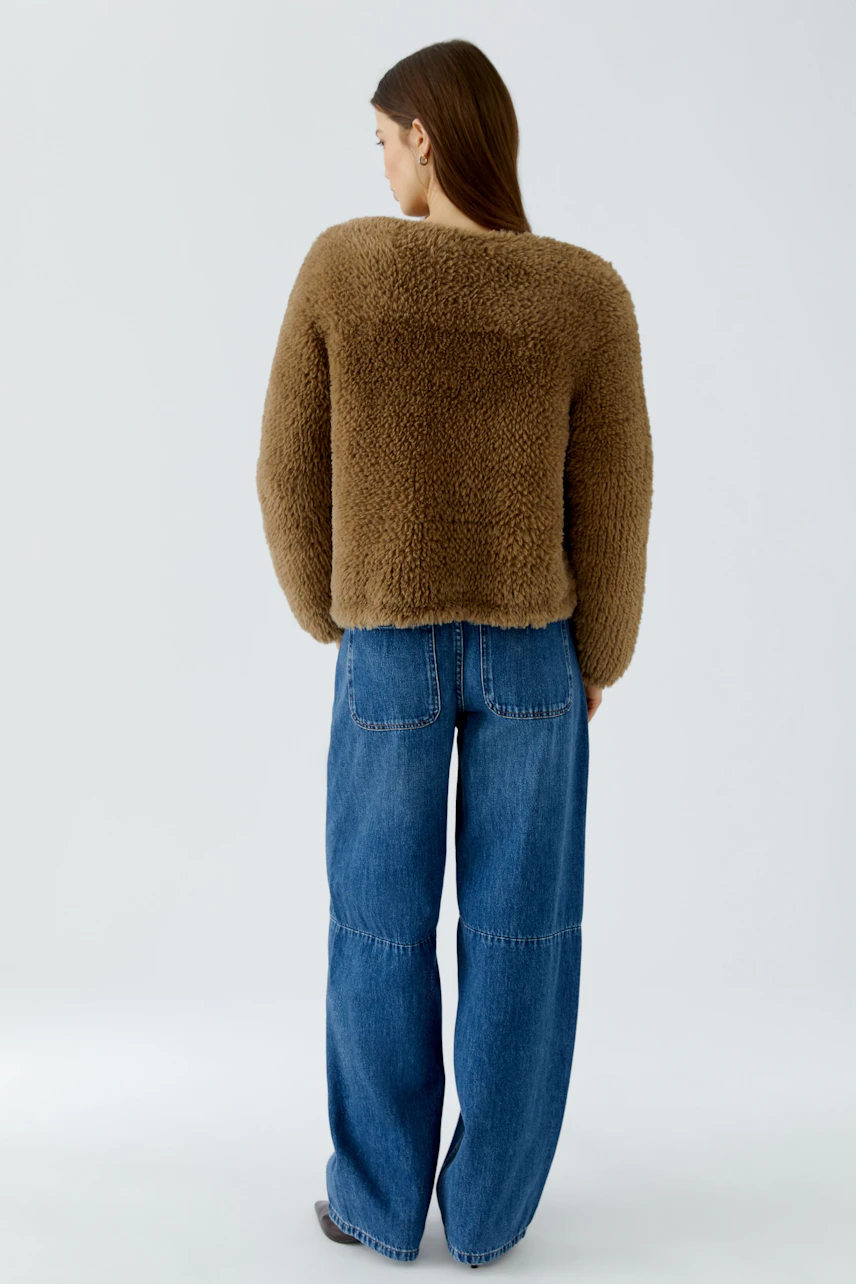 Woman in cozy brown cardigan, paired with relaxed blue jeans, standing confidently.