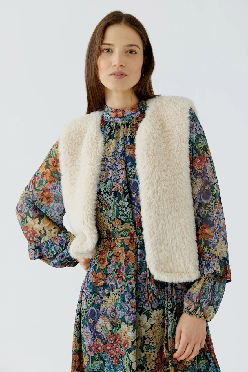 Woman in floral dress with cozy knit vest, looking relaxed and stylish.