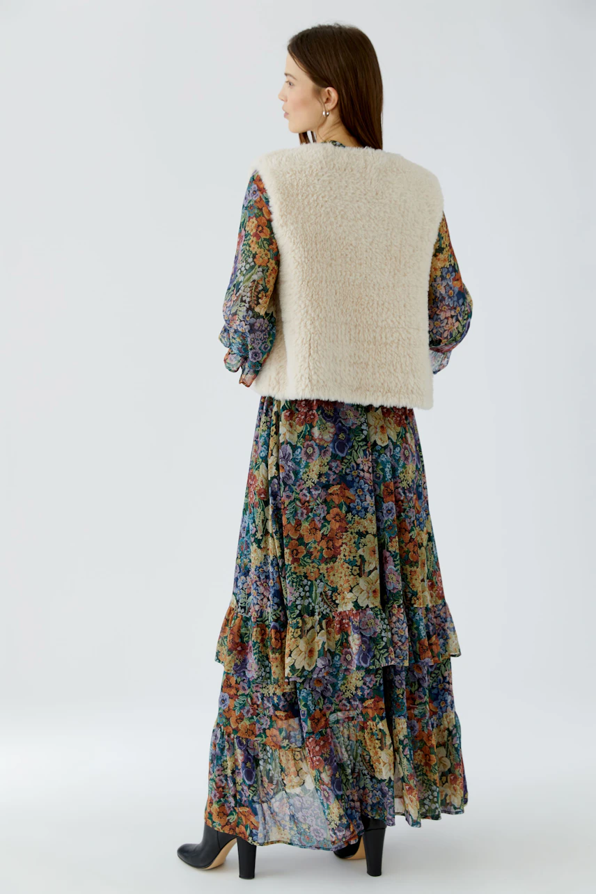 Woman in floral dress with a cozy knit vest, looking to the side. Casual and stylish outfit.
