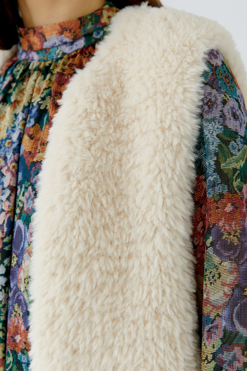 Woman in a floral dress with a cozy knit vest, showcasing a textured, warm layer.