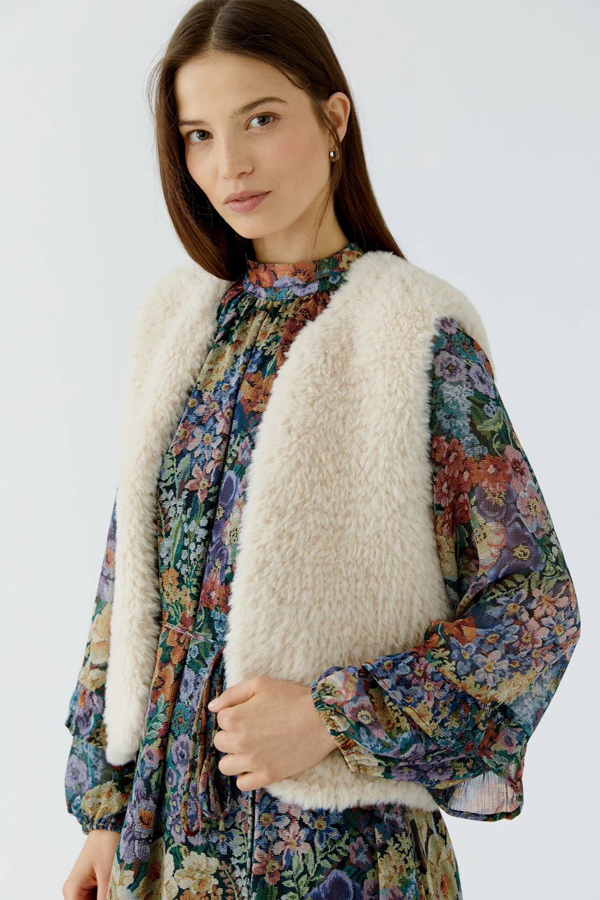 Woman in floral dress with cozy knit vest, looking confidently. Ideal for layering in cooler weather.