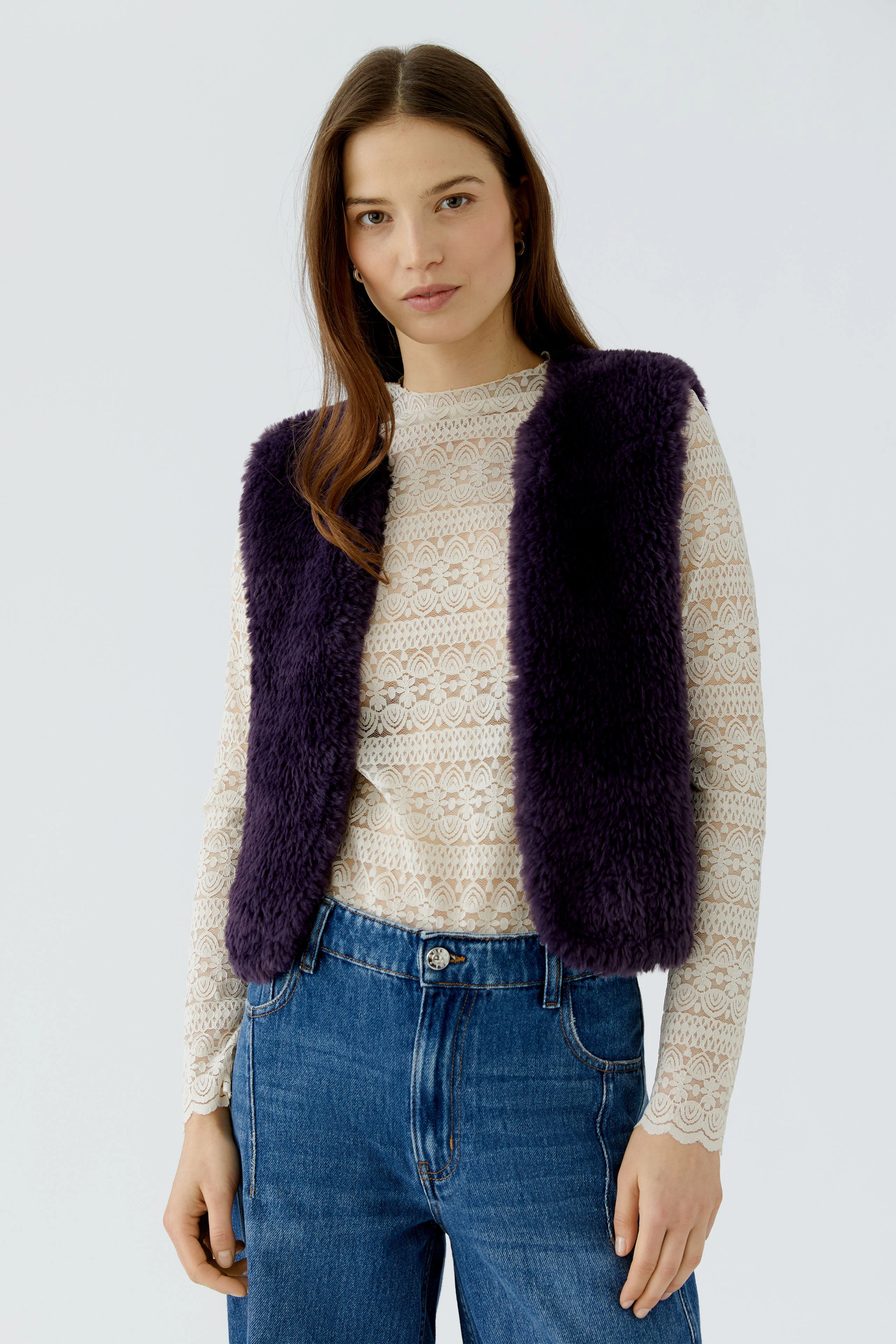 Woman in a purple knit vest over a lace top and jeans, showcasing casual style.
