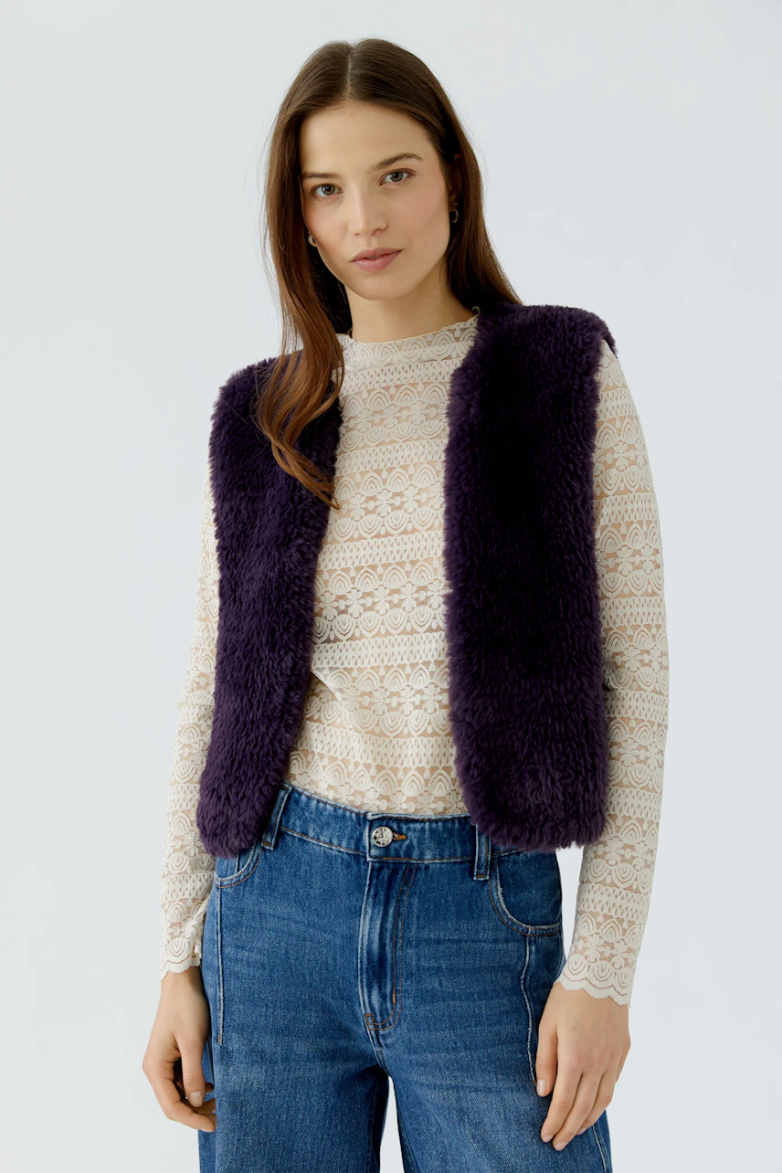 Woman in a purple knit vest over a lace top and jeans, showcasing casual style.