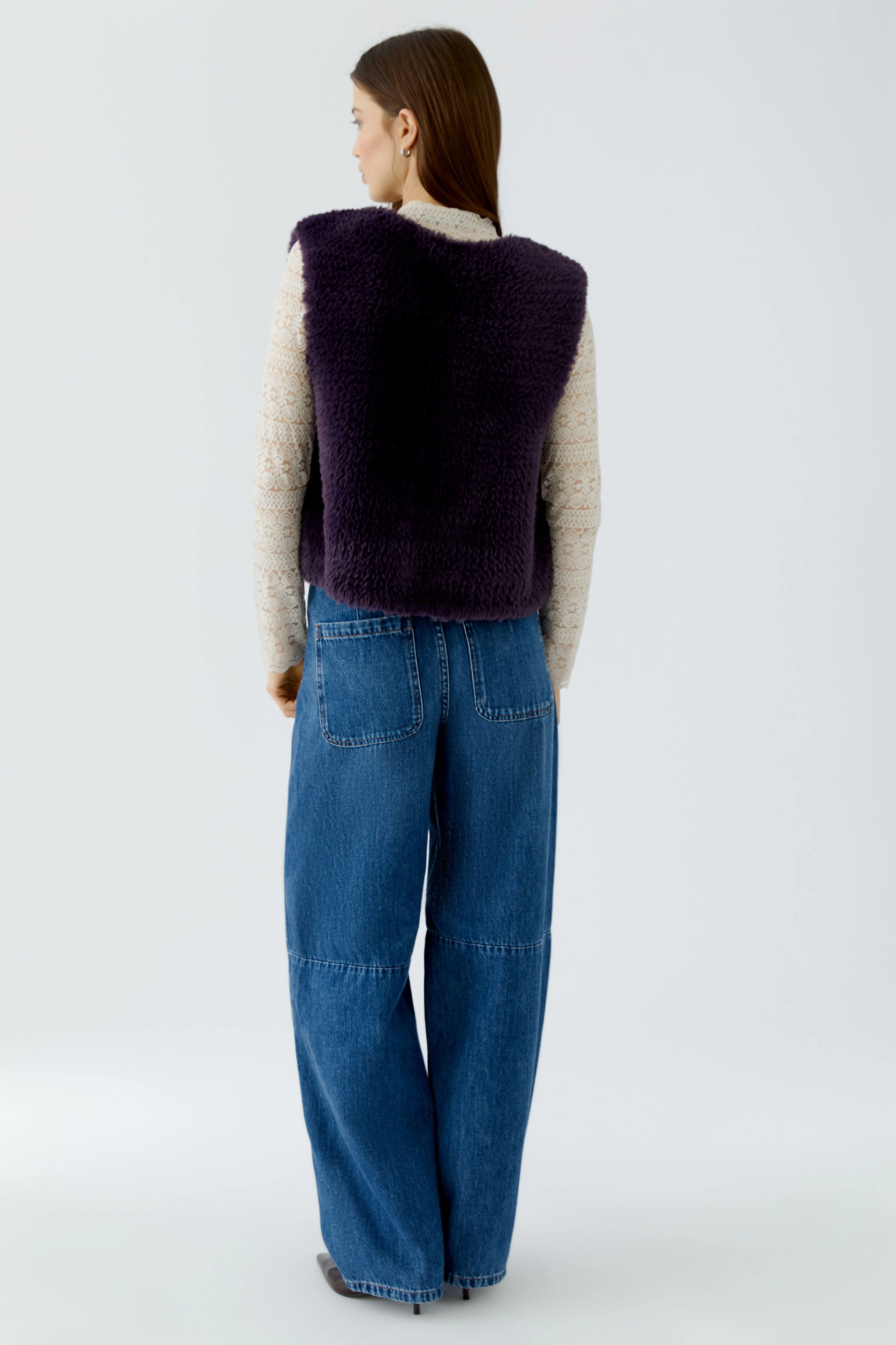 Woman in a purple knit vest over a beige top and wide-leg jeans, viewed from the back.