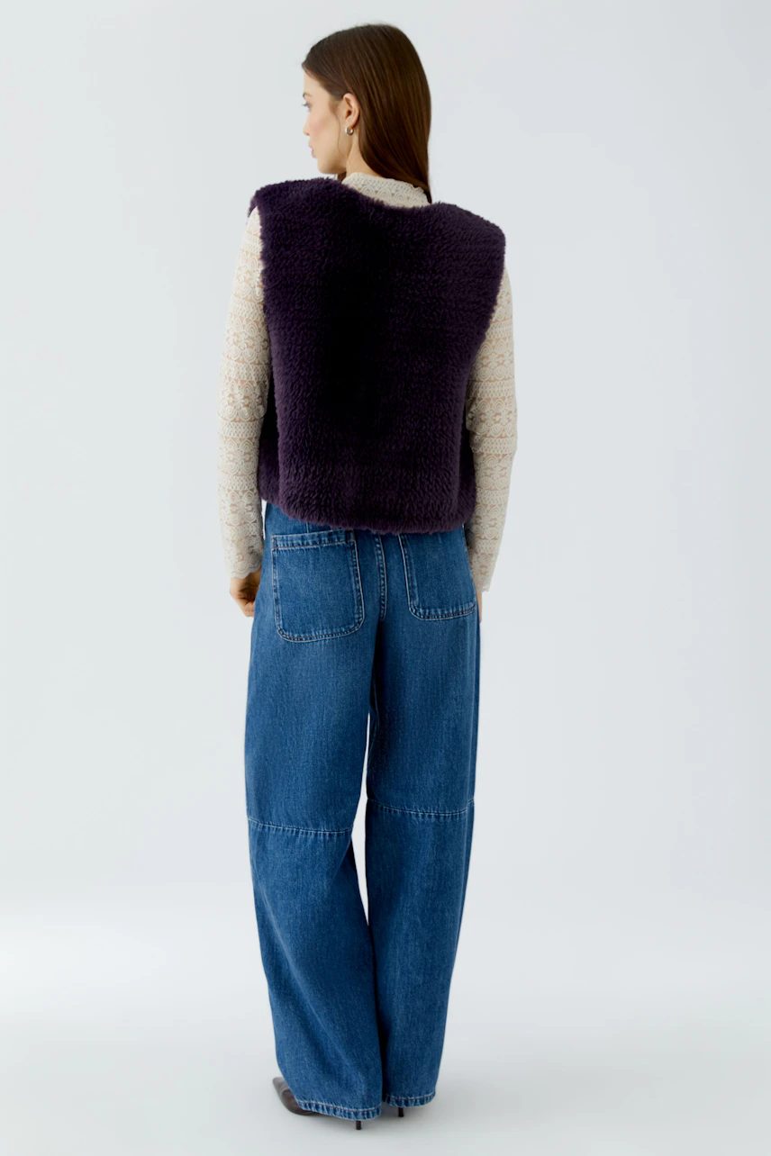 Woman in a purple knit vest over a beige top and wide-leg jeans, viewed from the back.