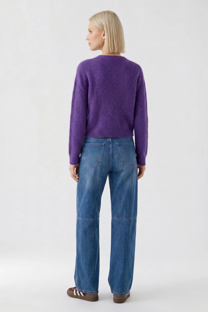 Lässiger Damen-Pullover: Frau im lila Pullover und blauer Jeans, von hinten gesehen, mit blonden Haaren.
