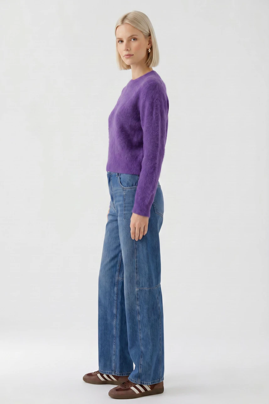 Lässiger Damen-Pullover: Frau im lila Pullover und blauer Jeans, seitlich stehend, mit entspanntem Ausdruck.