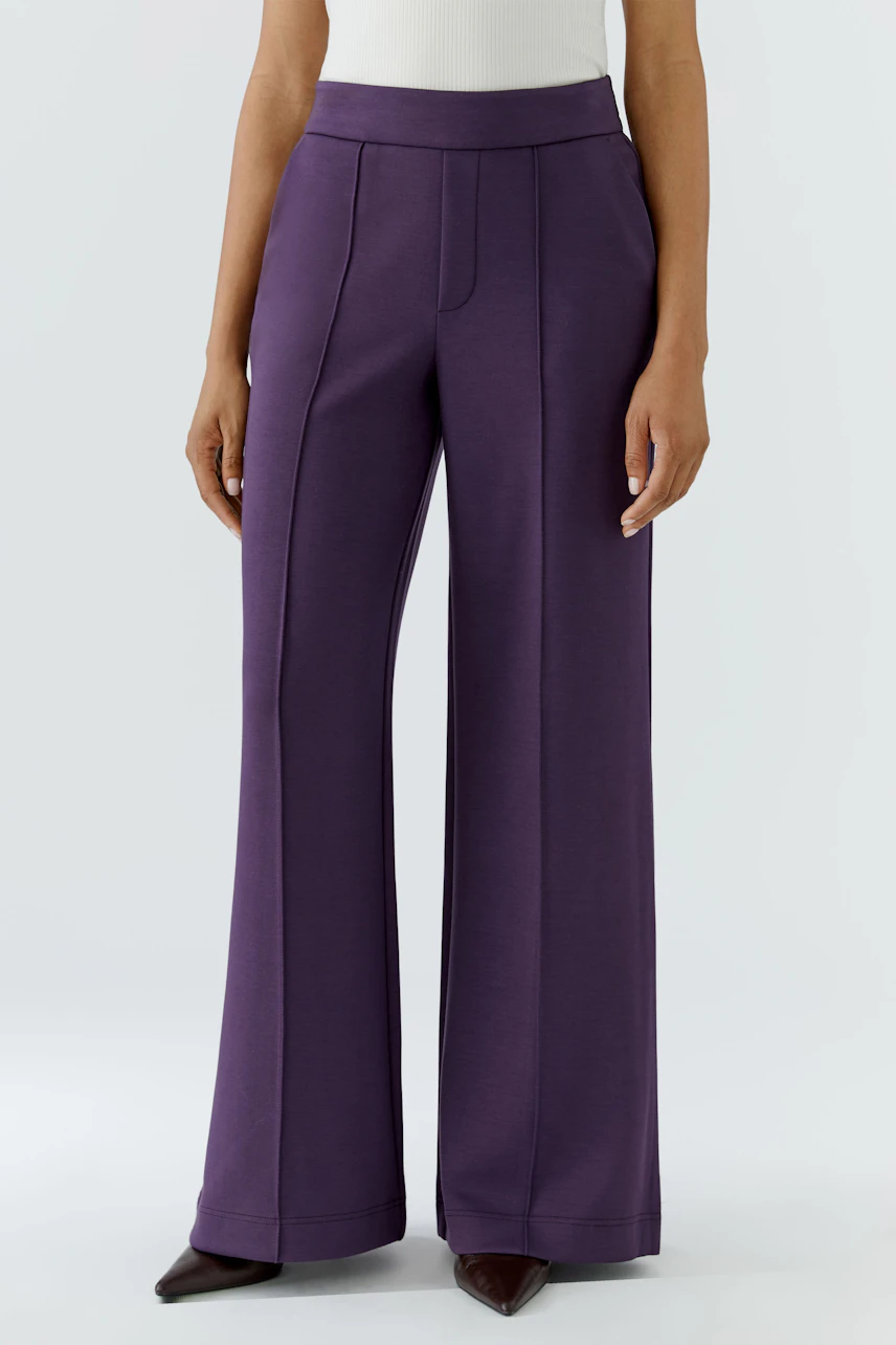 Woman in purple wide-leg pants, standing confidently. The pants have a high waist and sleek design.