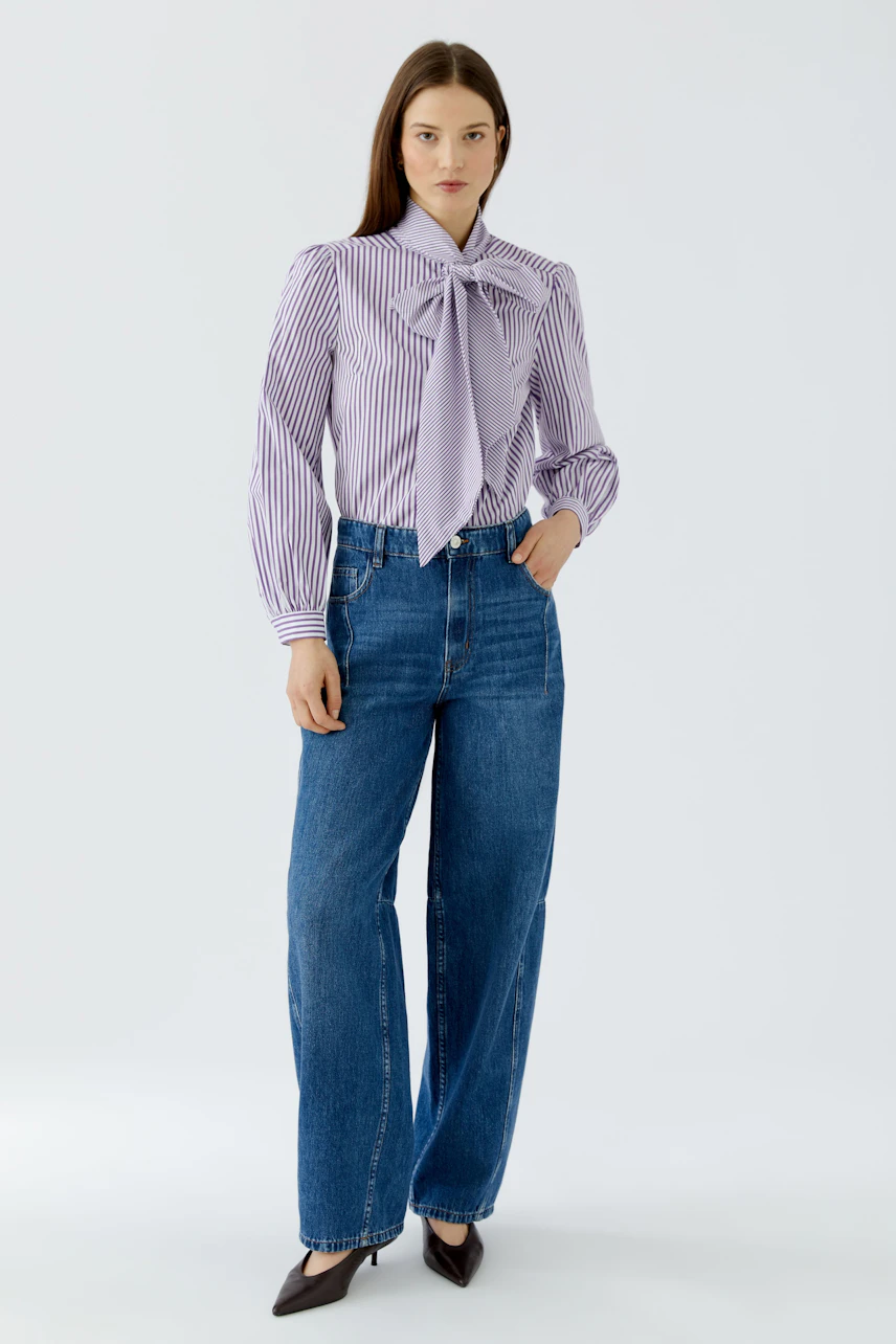 Frau in gestreifter Schluppenbluse und blauer Jeans, steht selbstbewusst. Lässiger Look für jeden Anlass.
