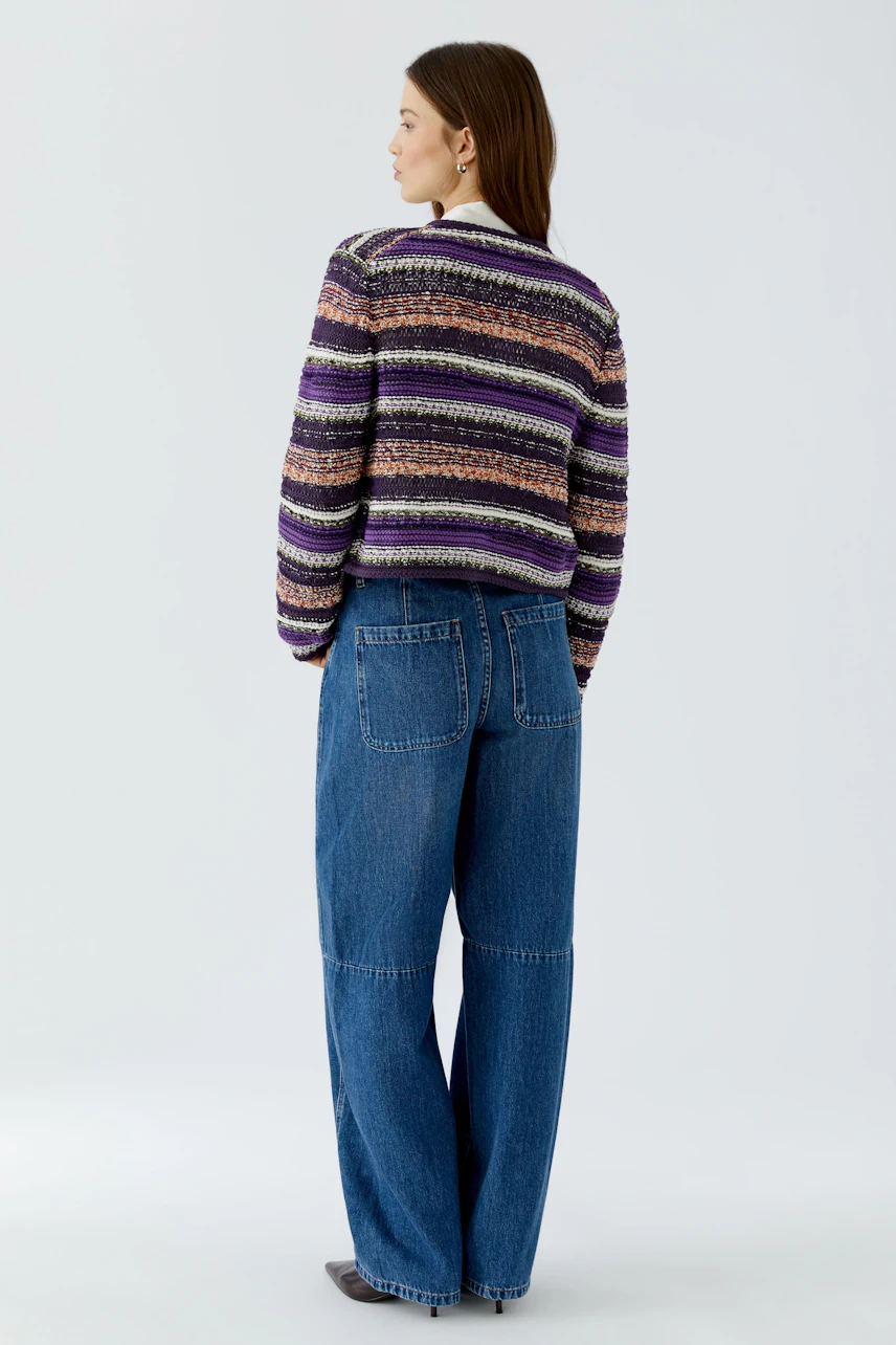 Frau in bunter Strickjacke und blauer Jeans, von hinten gesehen. Lässiger Look für den Alltag.