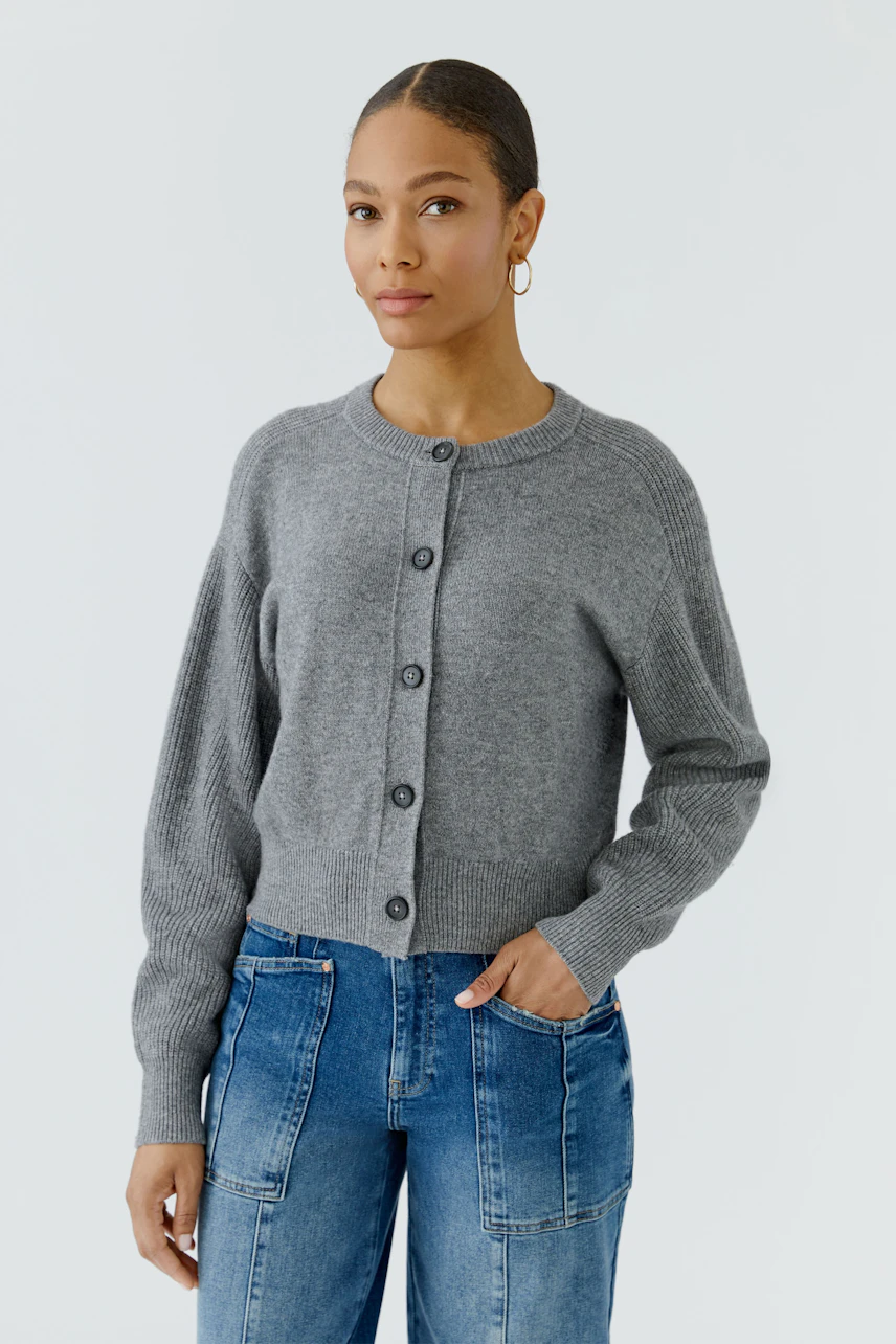 Casual cardigan: Woman in a grey knit cardigan with button front, paired with blue jeans, looks relaxed.