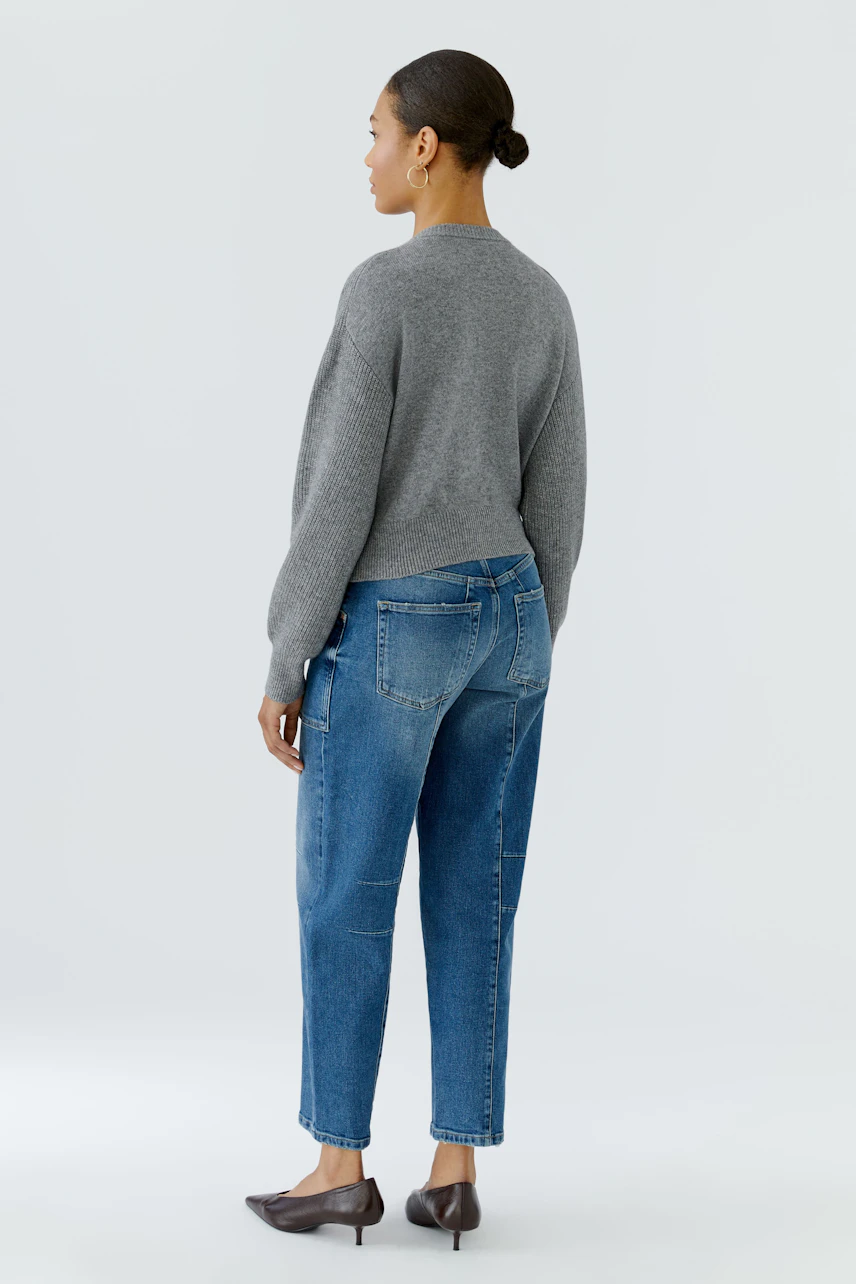 Casual cardigan: Woman in a grey knit cardigan and blue jeans, standing confidently.