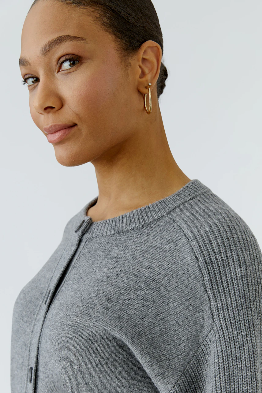 Casual women's cardigan: Woman in a grey knit cardigan with ribbed sleeves, looking confidently.