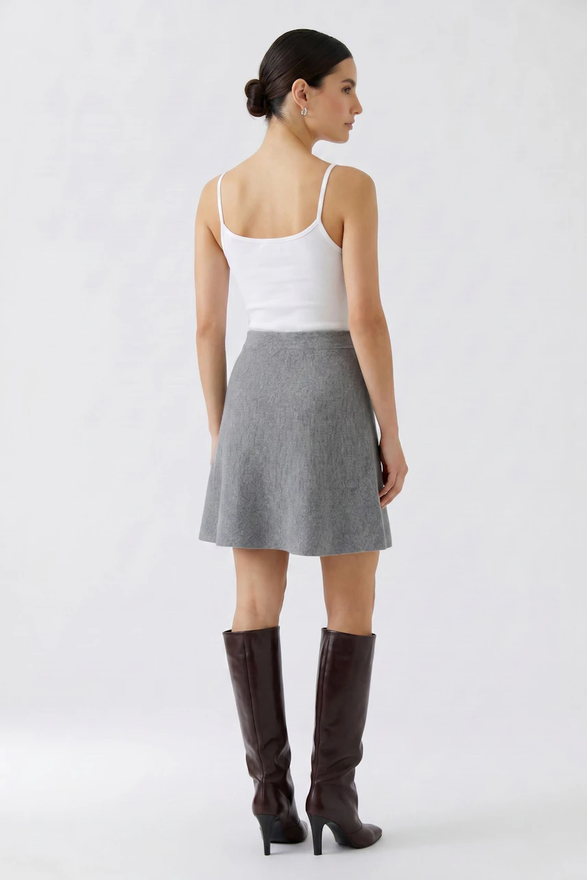 Knit skirt: Woman in a gray knit skirt, white tank top, and brown boots, viewed from the back.