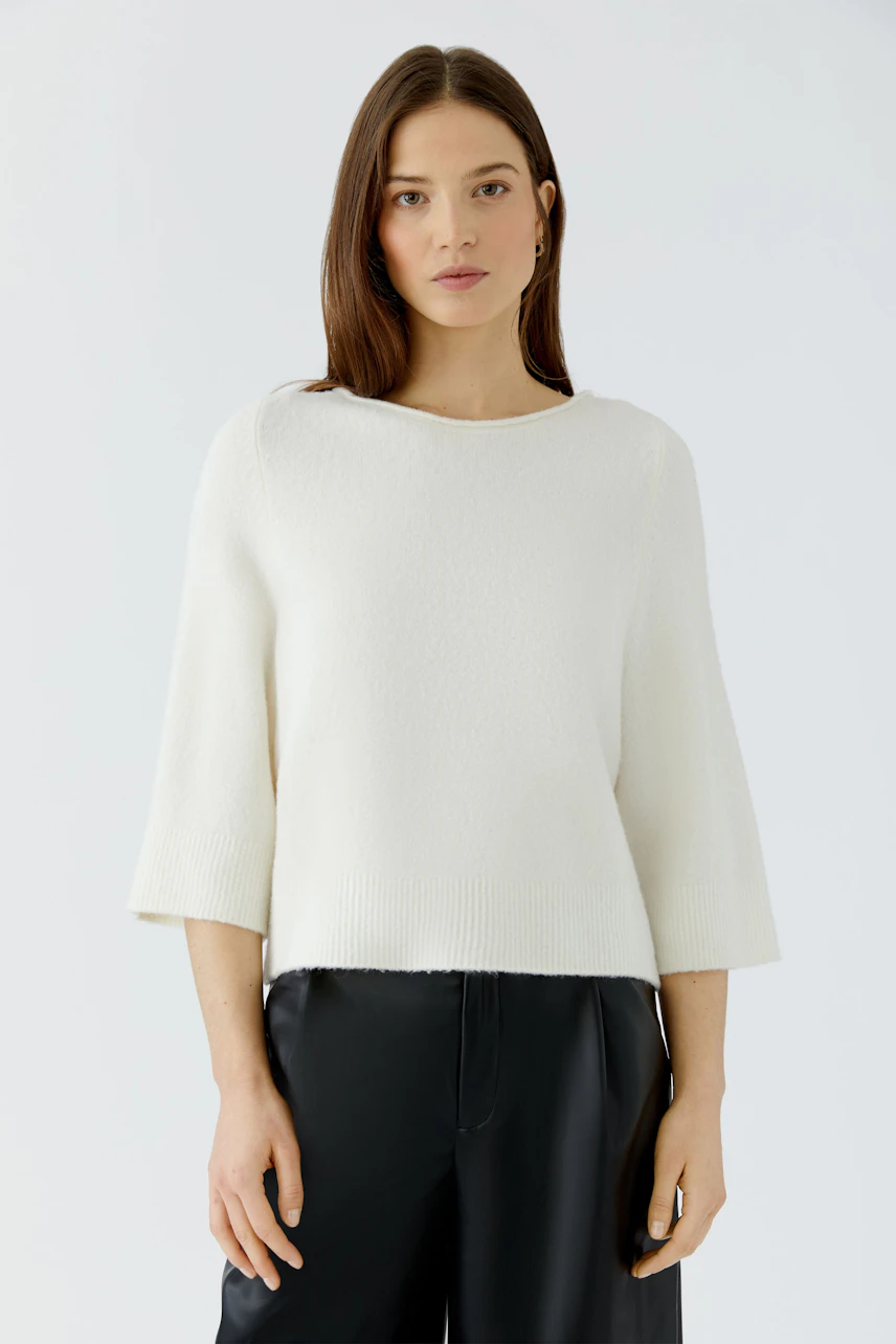 Casual women's pullover: Woman in a white pullover with wide sleeves and black pants, looking poised.