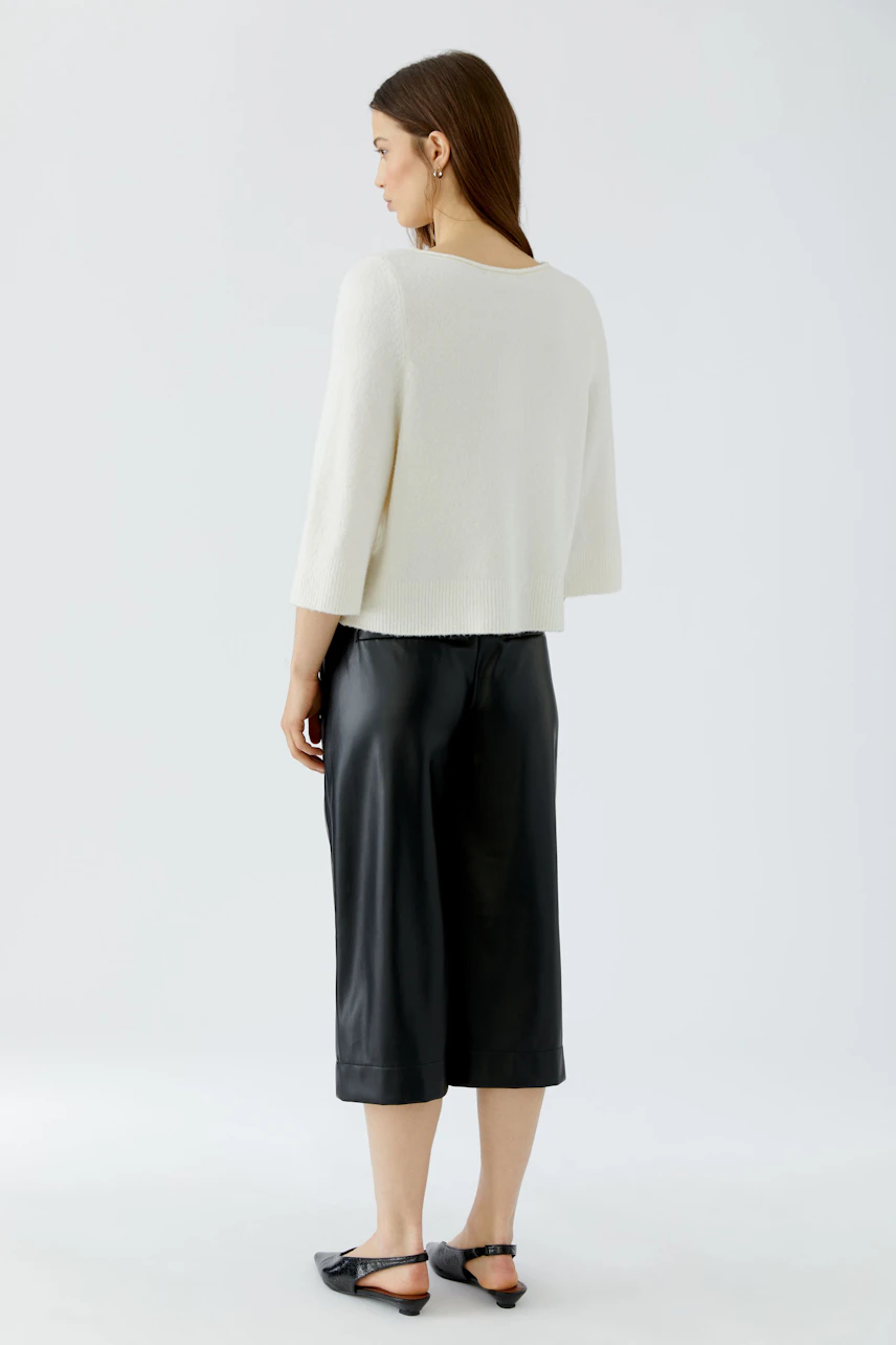 Casual women's pullover: Woman in a white pullover and black culottes, standing confidently.