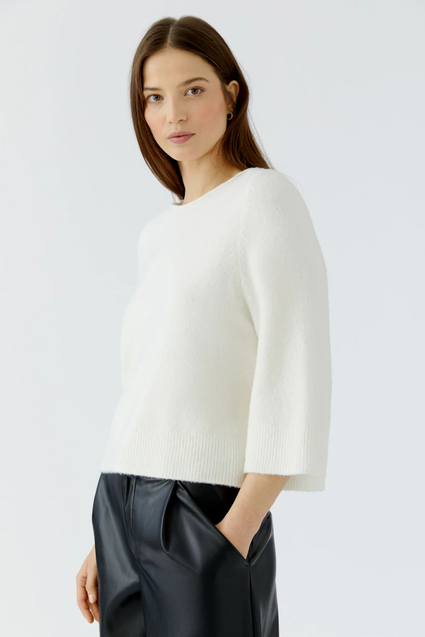 Casual women's pullover: Woman in a white pullover with 3/4 sleeves and black pants, looking relaxed.