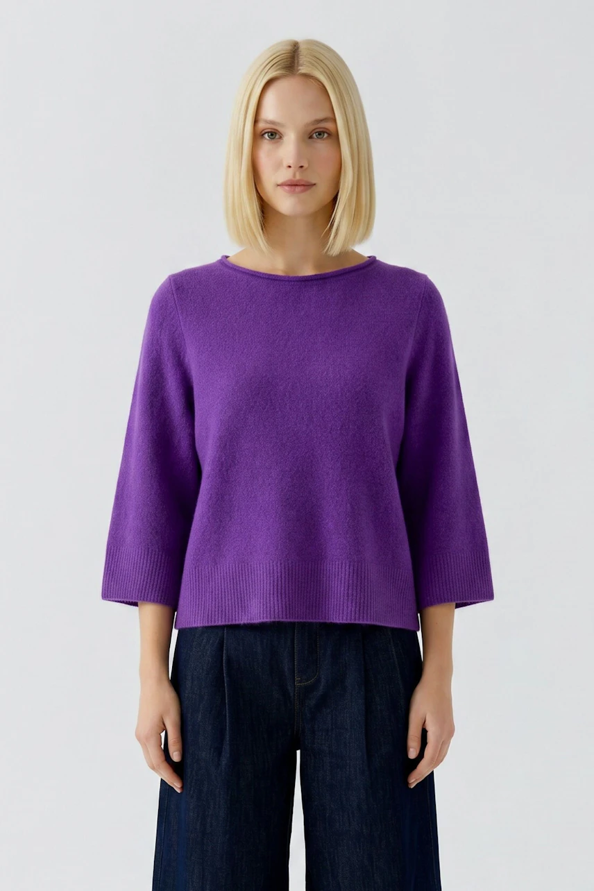 Frau im lila Pullover mit 3/4-Ärmeln, kombiniert mit dunkler Jeans. Schlichtes, modernes Design.