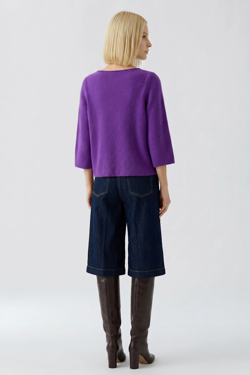 Frau im lila Pullover, kombiniert mit Jeans-Culottes und kniehohen Stiefeln, von hinten gesehen.