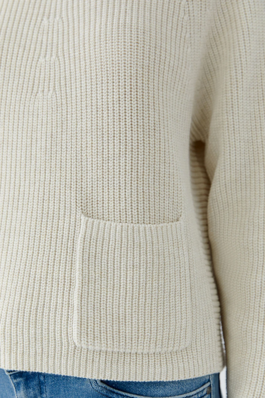 Beiger Damen-Pullover: Grob gestrickter Pullover mit aufgesetzter Tasche, kombiniert mit blauer Jeans.