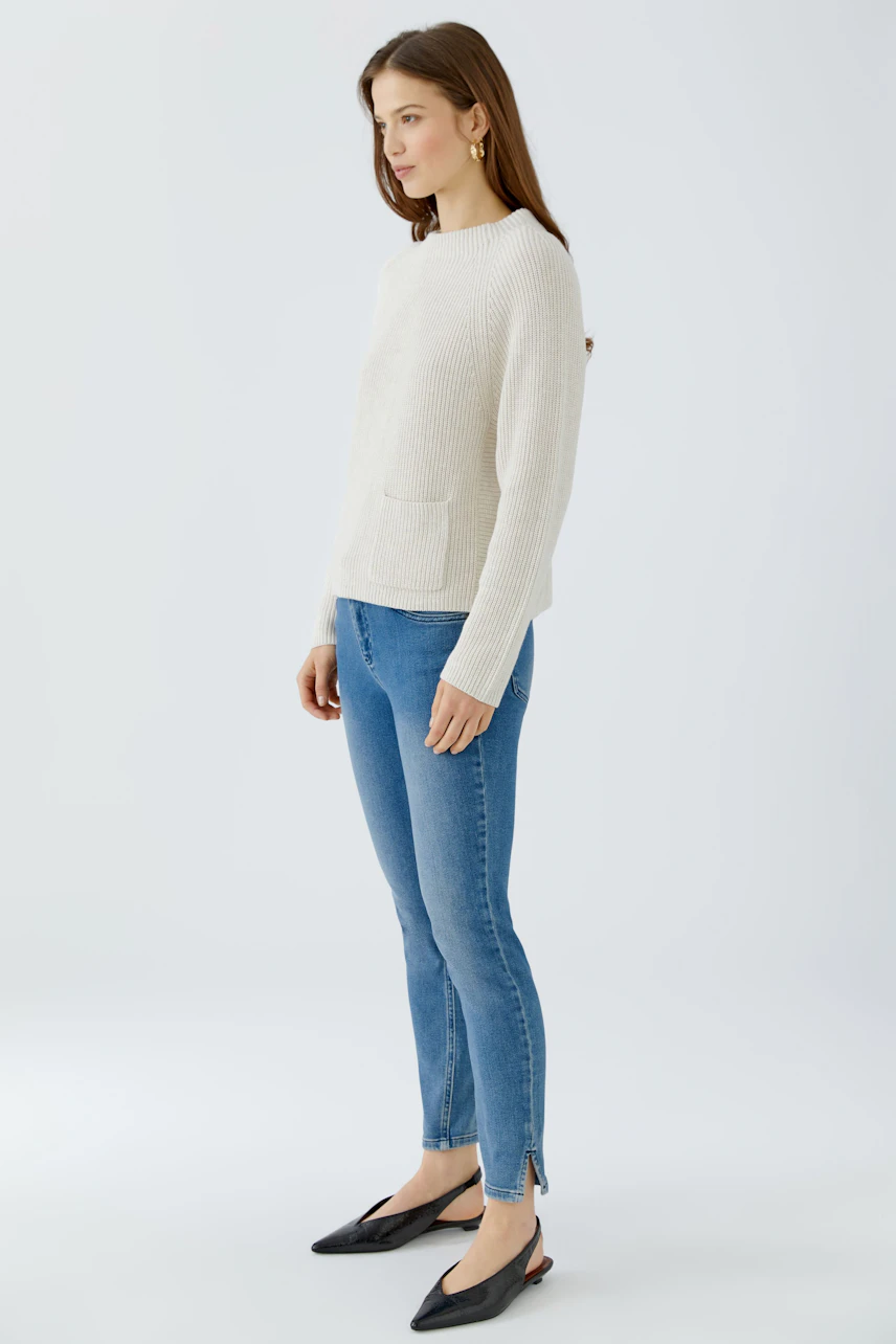 Lässiger Damen-Pullover: Frau im cremefarbenen Pullover und blauen Jeans, seitlich stehend.