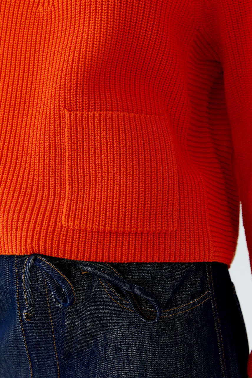 Roter Damen-Pullover: Strickpullover mit Tasche, kombiniert mit dunkelblauer Hose.