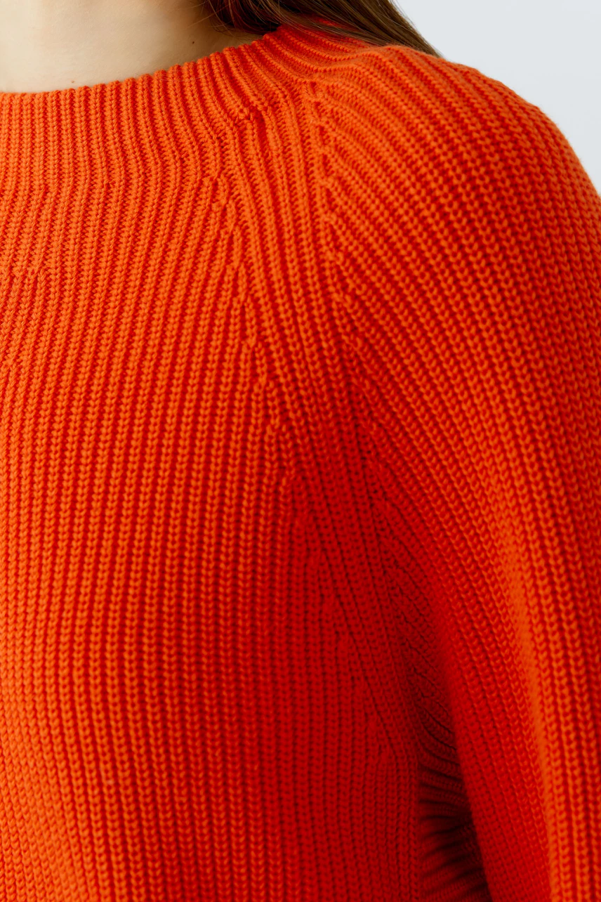 Strukturierter Damen-Pullover: Frau trägt leuchtend orangefarbenen Strickpullover mit Zopfmuster.