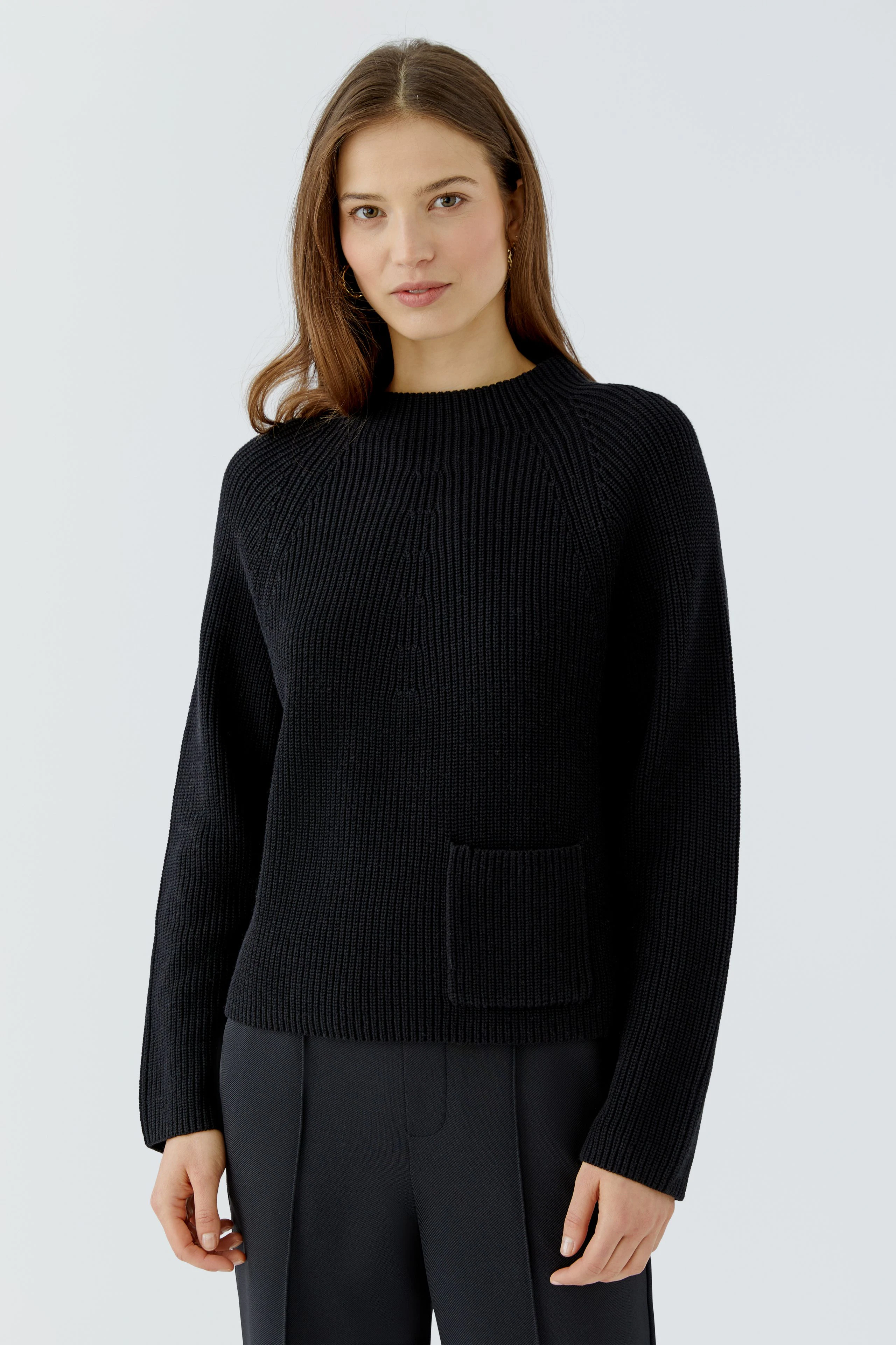 Casual women's pullover: Woman in a black knit pullover with a front pocket, paired with dark trousers.