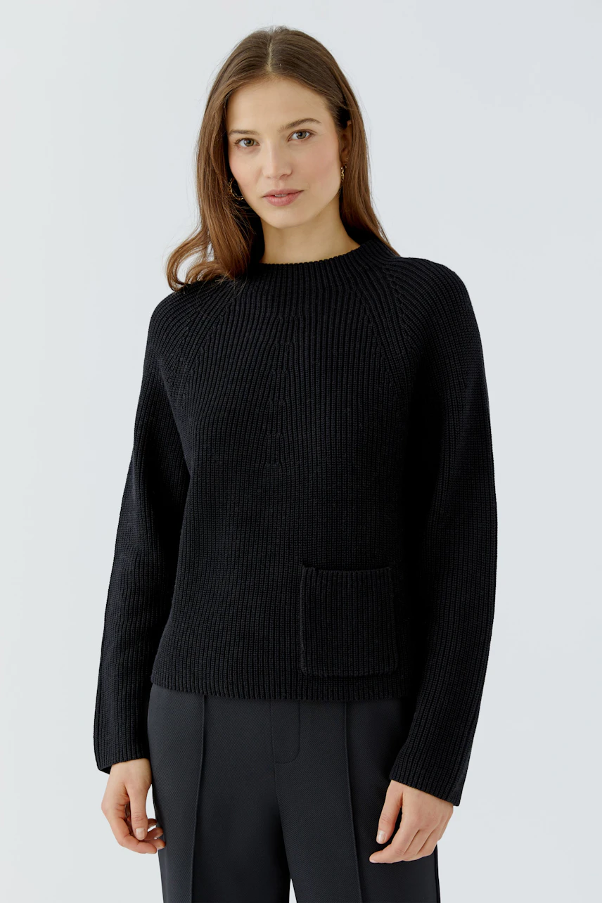 Casual women's pullover: Woman in a black knit pullover with a front pocket, paired with dark trousers.