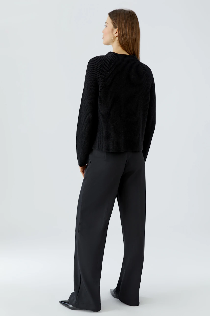Casual women's pullover: Woman in a black pullover and wide-leg pants, viewed from the back.