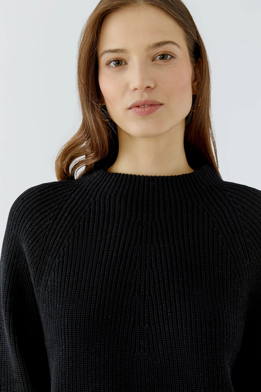 Casual women's pullover: Woman in a black knit pullover with a relaxed fit, looking confidently ahead.