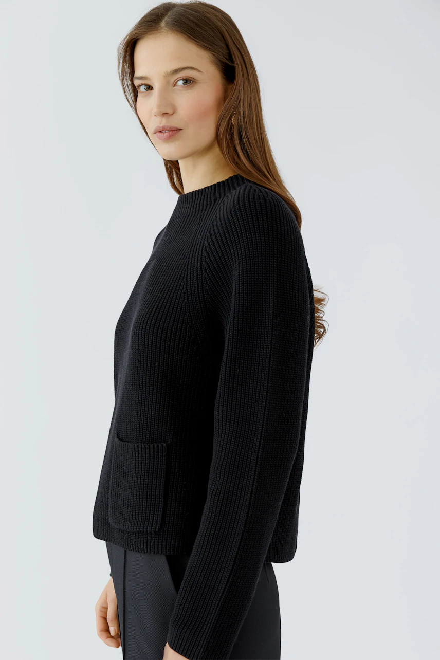 Woman in a black pullover with a simple design, standing confidently.
