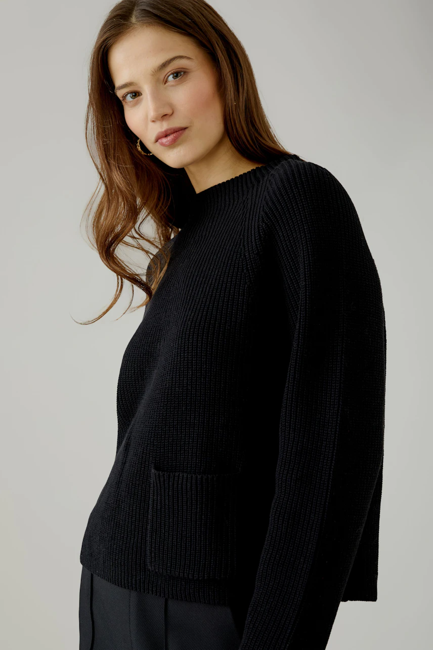 Casual women's pullover: Woman in a black knit pullover with a relaxed fit, looking confidently.