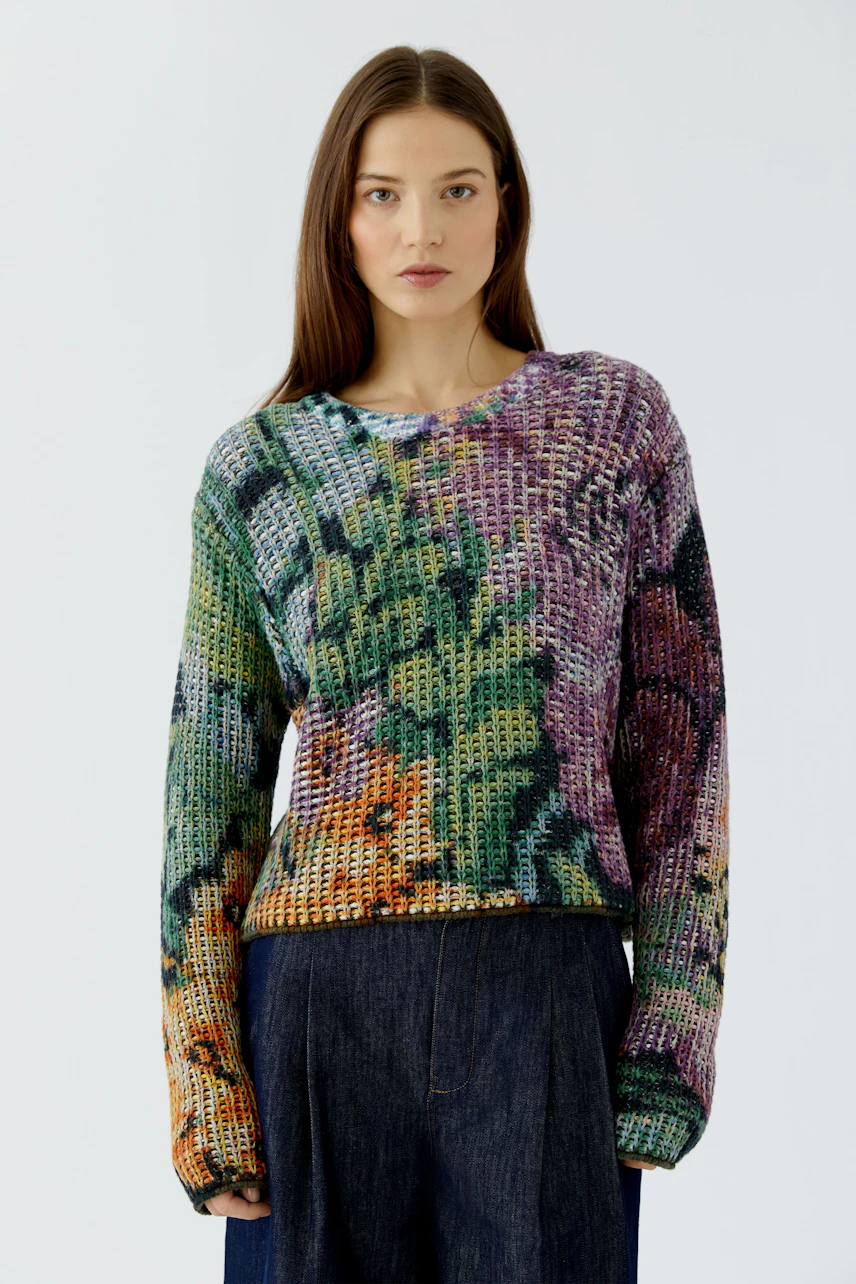 Colorful women's pullover: Woman in a vibrant knit pullover with abstract patterns, paired with dark jeans.