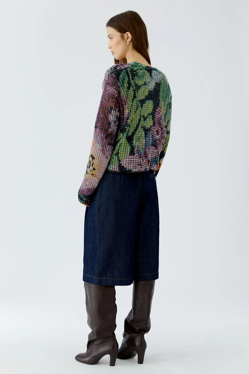 Casual pullover: Woman in a colorful knit pullover with floral pattern, paired with denim skirt and boots.