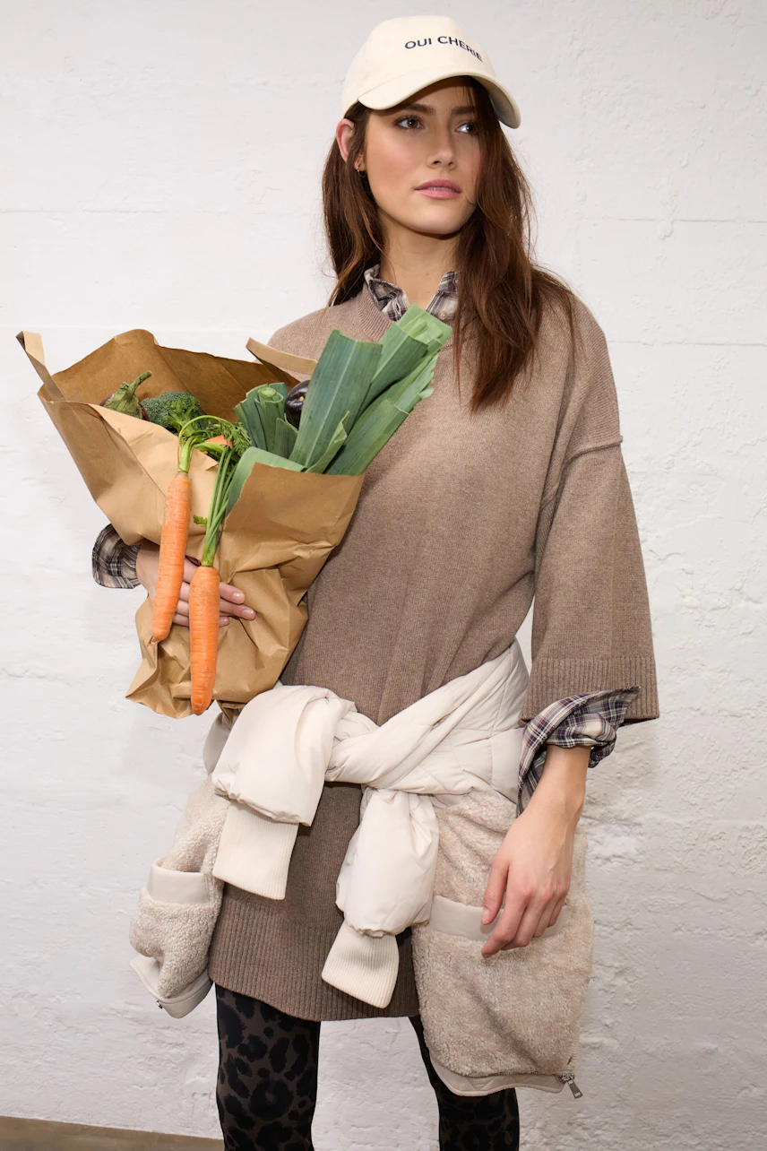 Casual women's pullover: Woman in a brown pullover with a cap, holding groceries, exudes relaxed style.