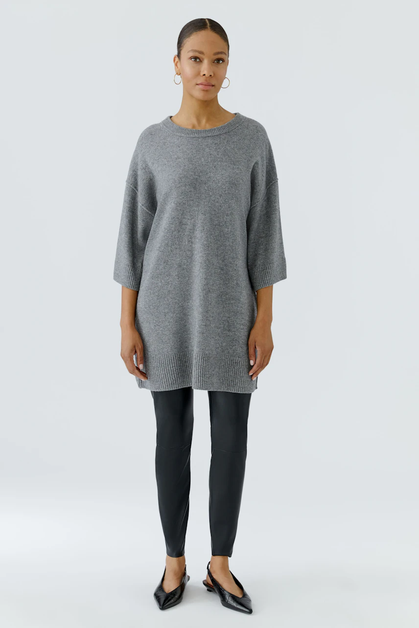 Casual women's pullover: Woman in a grey oversized pullover with black leggings and hoop earrings.