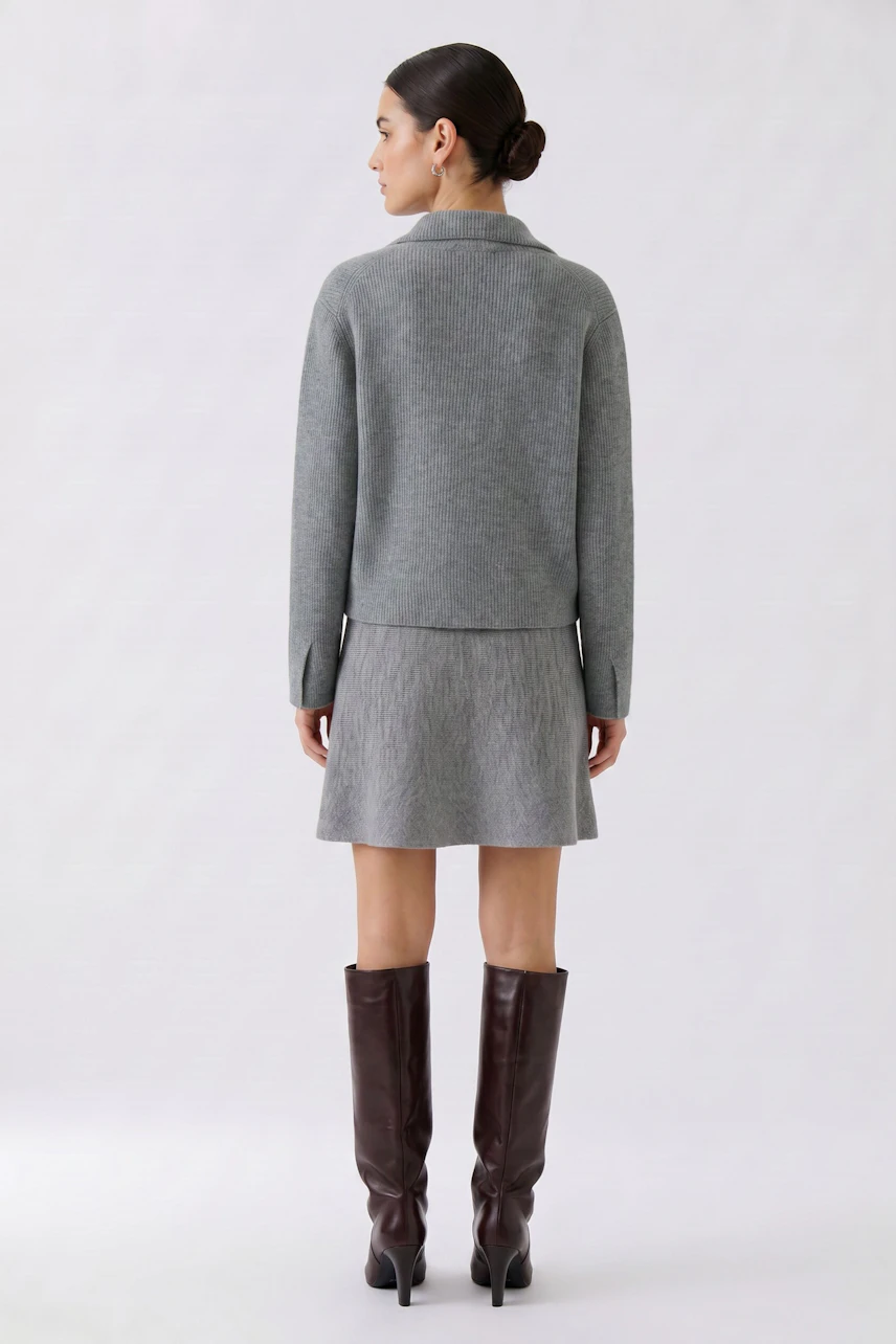 Woman in a gray cardigan, paired with a matching skirt and brown boots, viewed from the back.