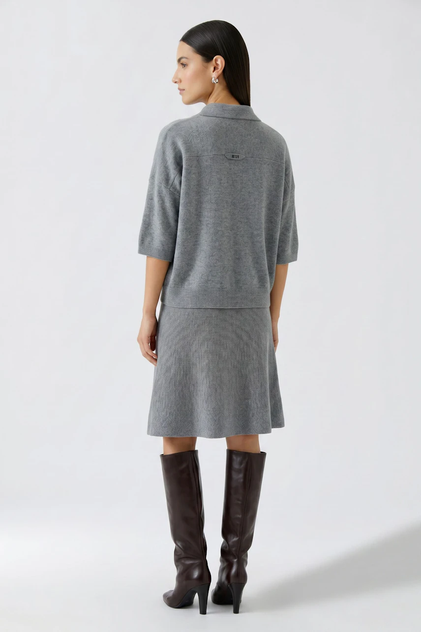 Woman in a grey pullover and skirt, viewed from the back, wearing tall brown boots.