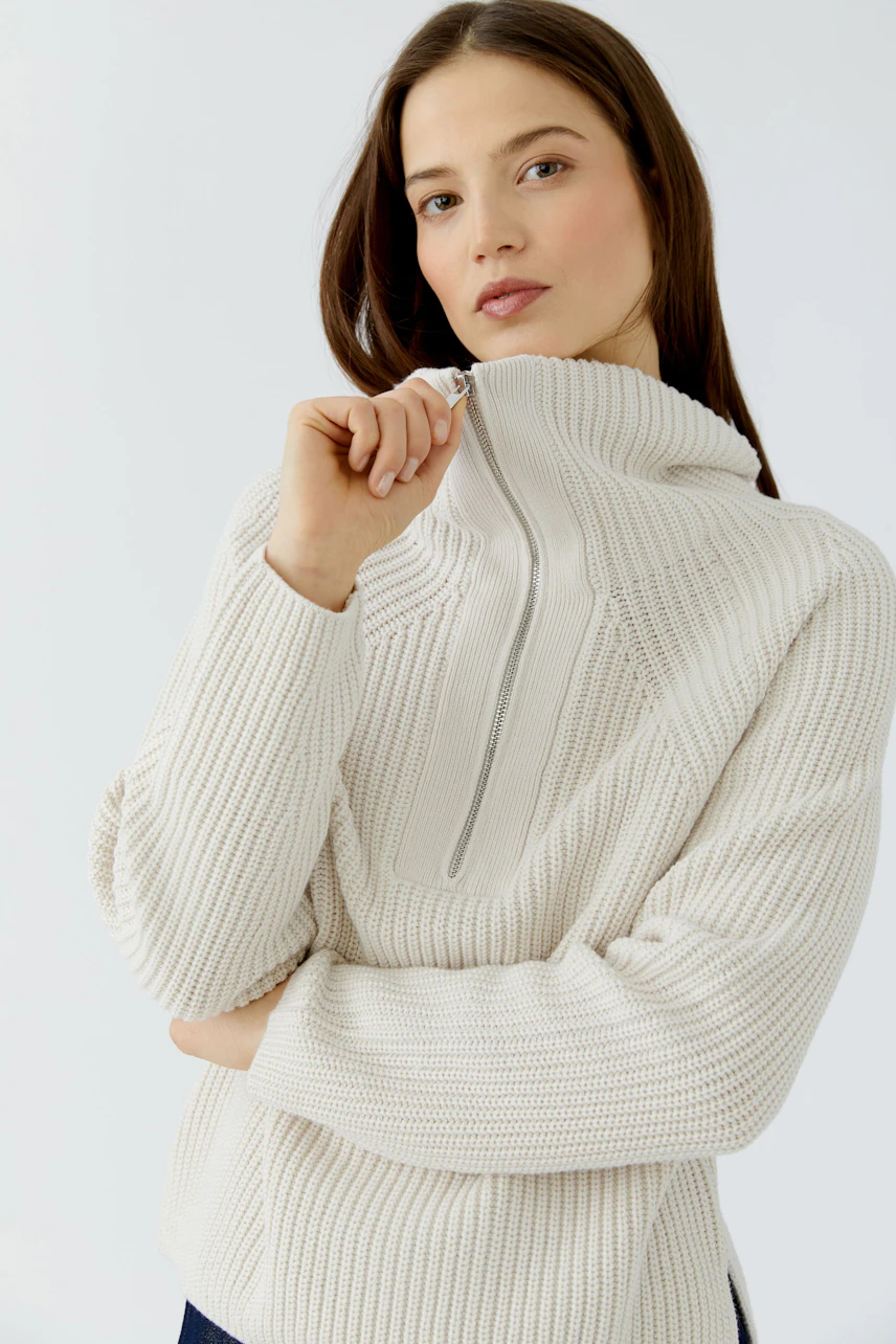 Frau im cremefarbenen Pullover mit Reißverschluss am Kragen, lässig und modern.
