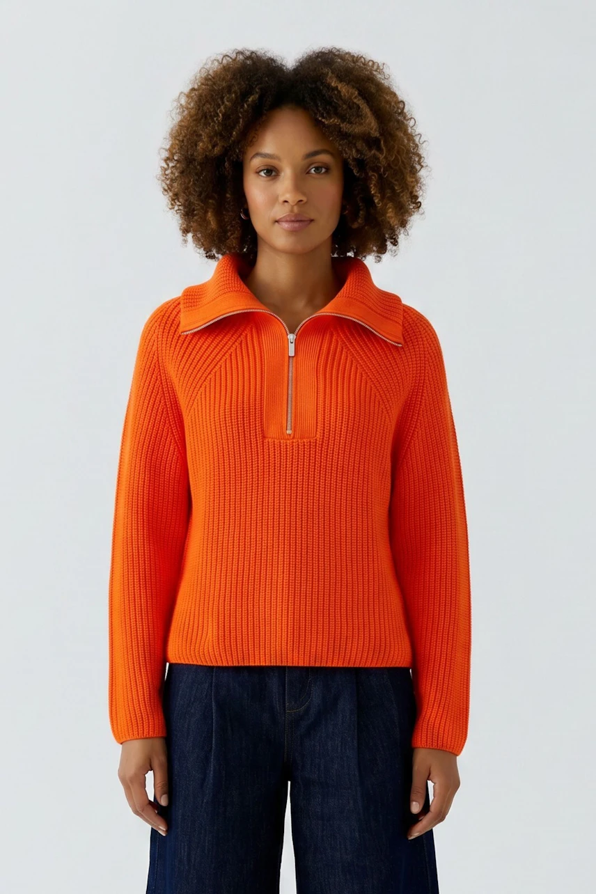 Bright orange pullover: Woman in a vibrant ribbed pullover with a zip collar, paired with dark jeans.