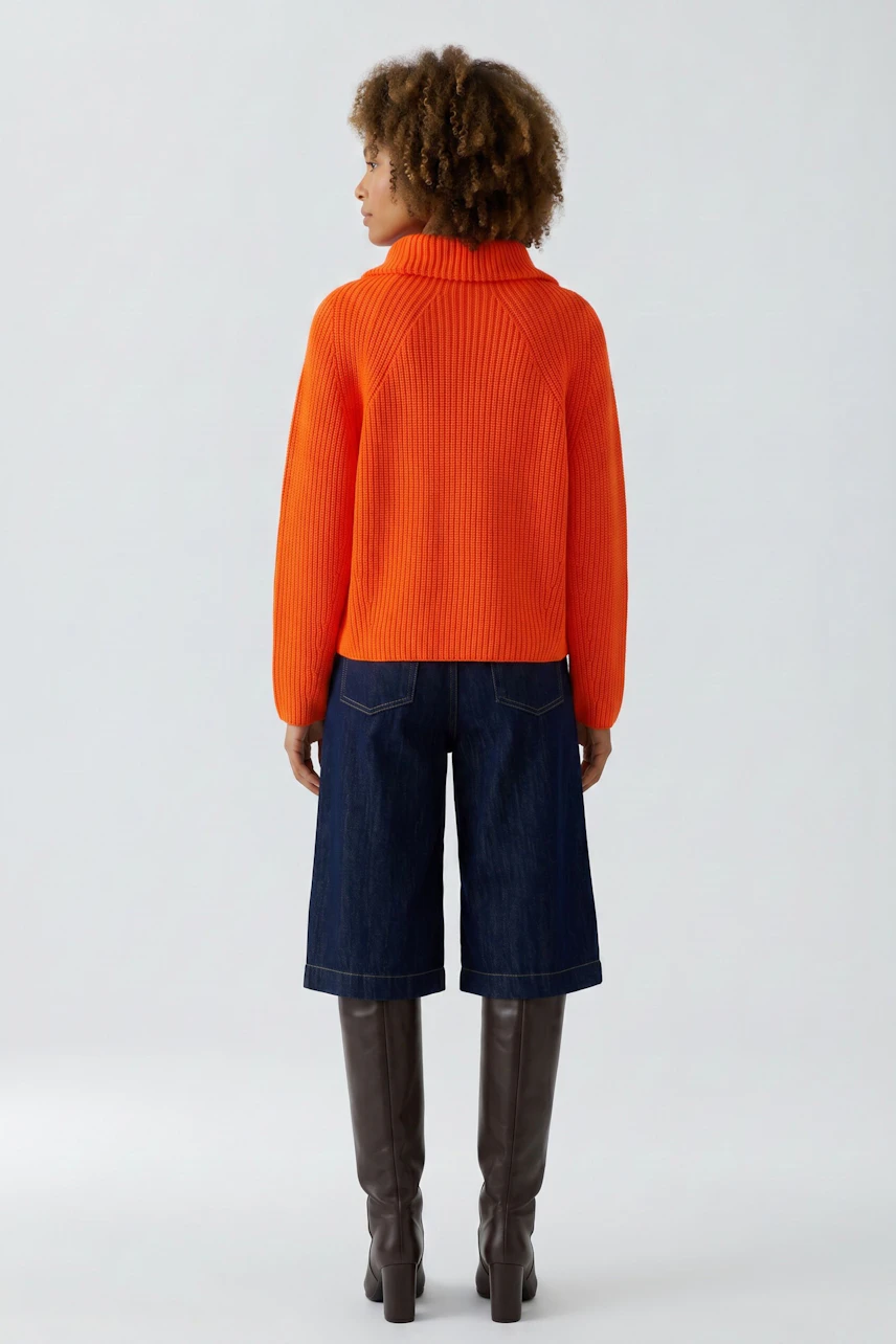 Woman in vibrant orange pullover, paired with denim culottes and knee-high boots, showcasing a casual look.