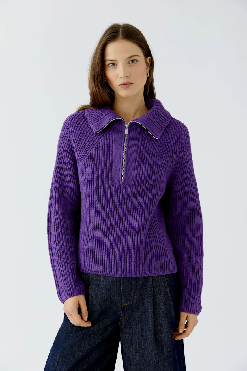 Casual women's pullover: Woman in a purple ribbed pullover with a zip collar, paired with dark jeans.