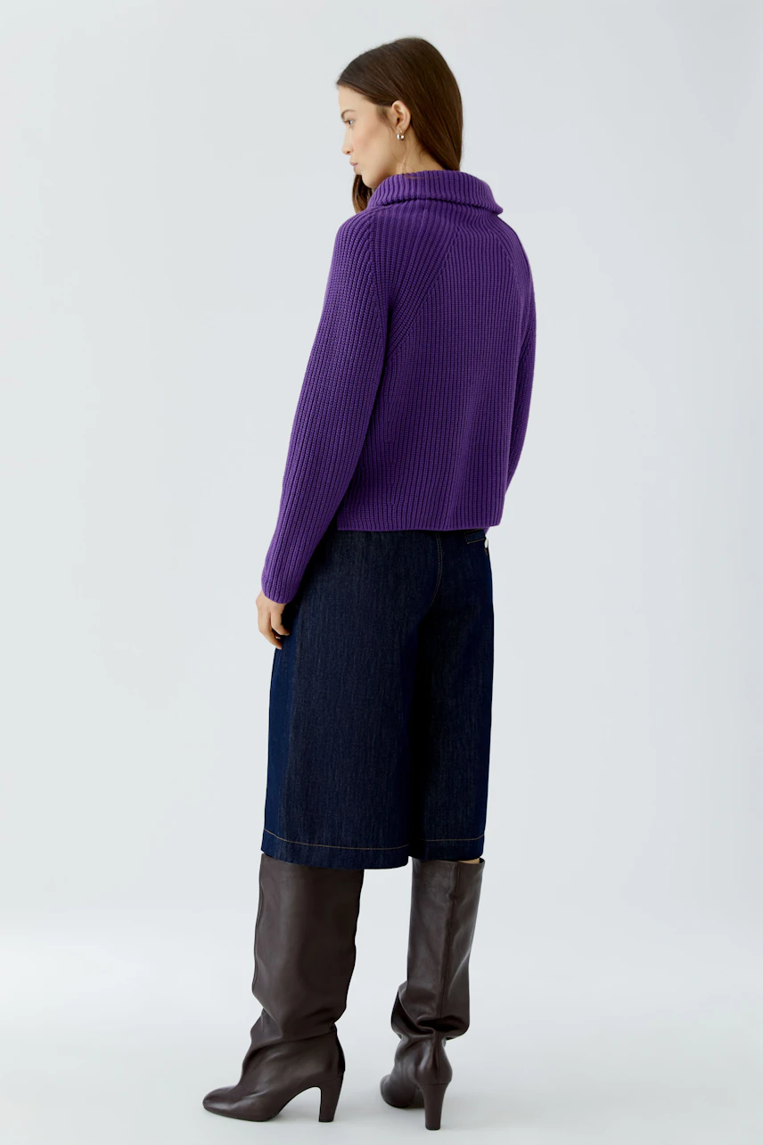 Casual women's pullover: Woman in purple pullover, denim culottes, and knee-high boots, facing sideways.