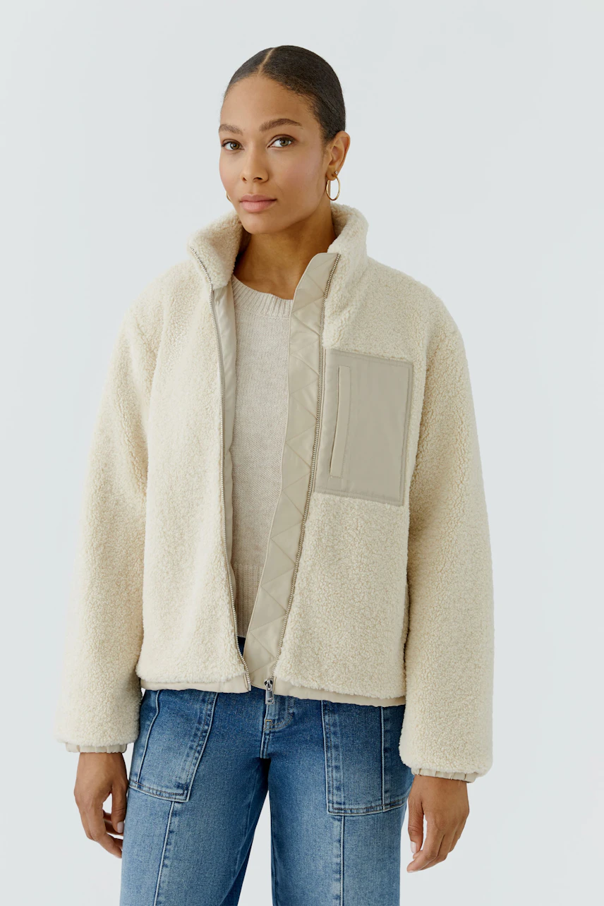 Casual blouson: Woman in cream fleece blouson with beige accents, paired with blue jeans, looks relaxed.