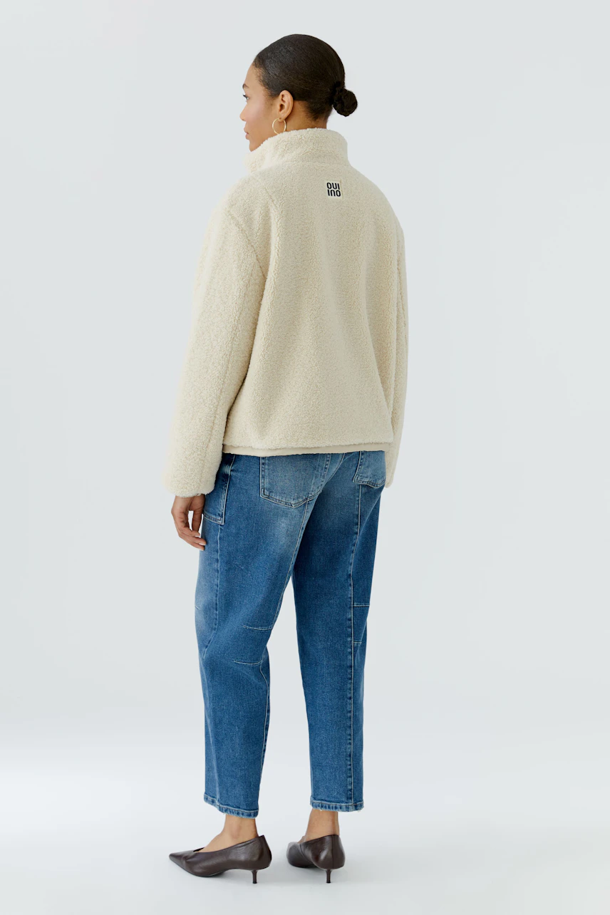 Casual blouson: Woman in cream blouson and blue jeans, standing with a relaxed posture.