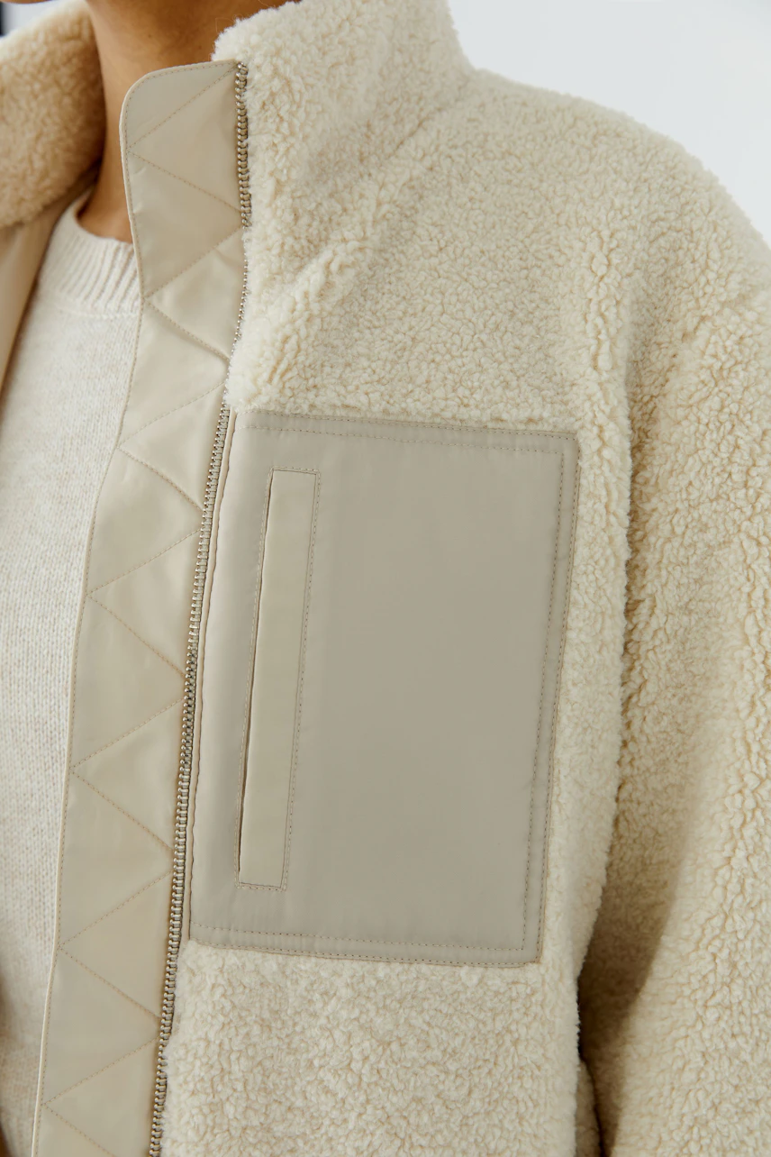 Cozy blouson: Woman in a cream fleece blouson with quilted details and a soft pullover underneath.