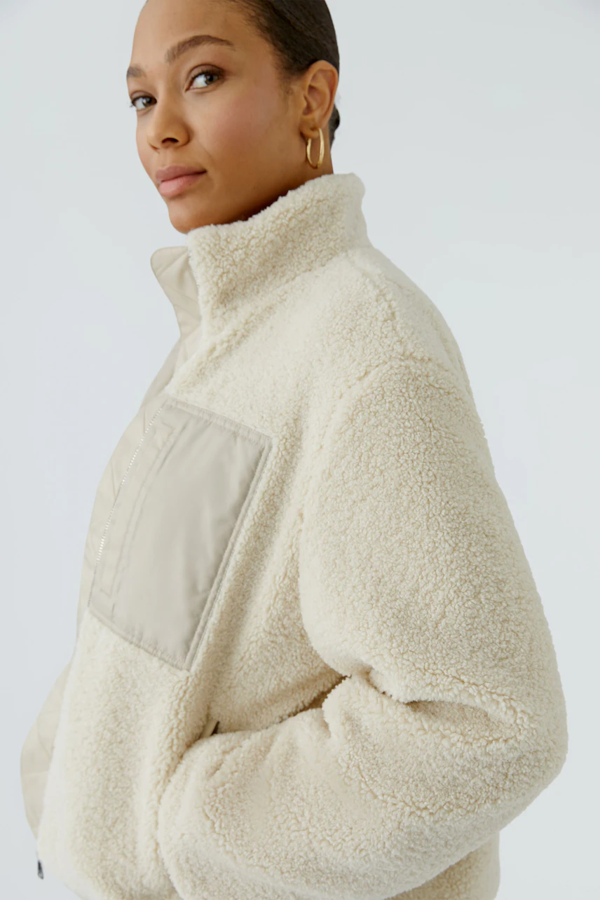 Woman in cozy beige blouson with high collar and pocket detail, exuding warmth and style.