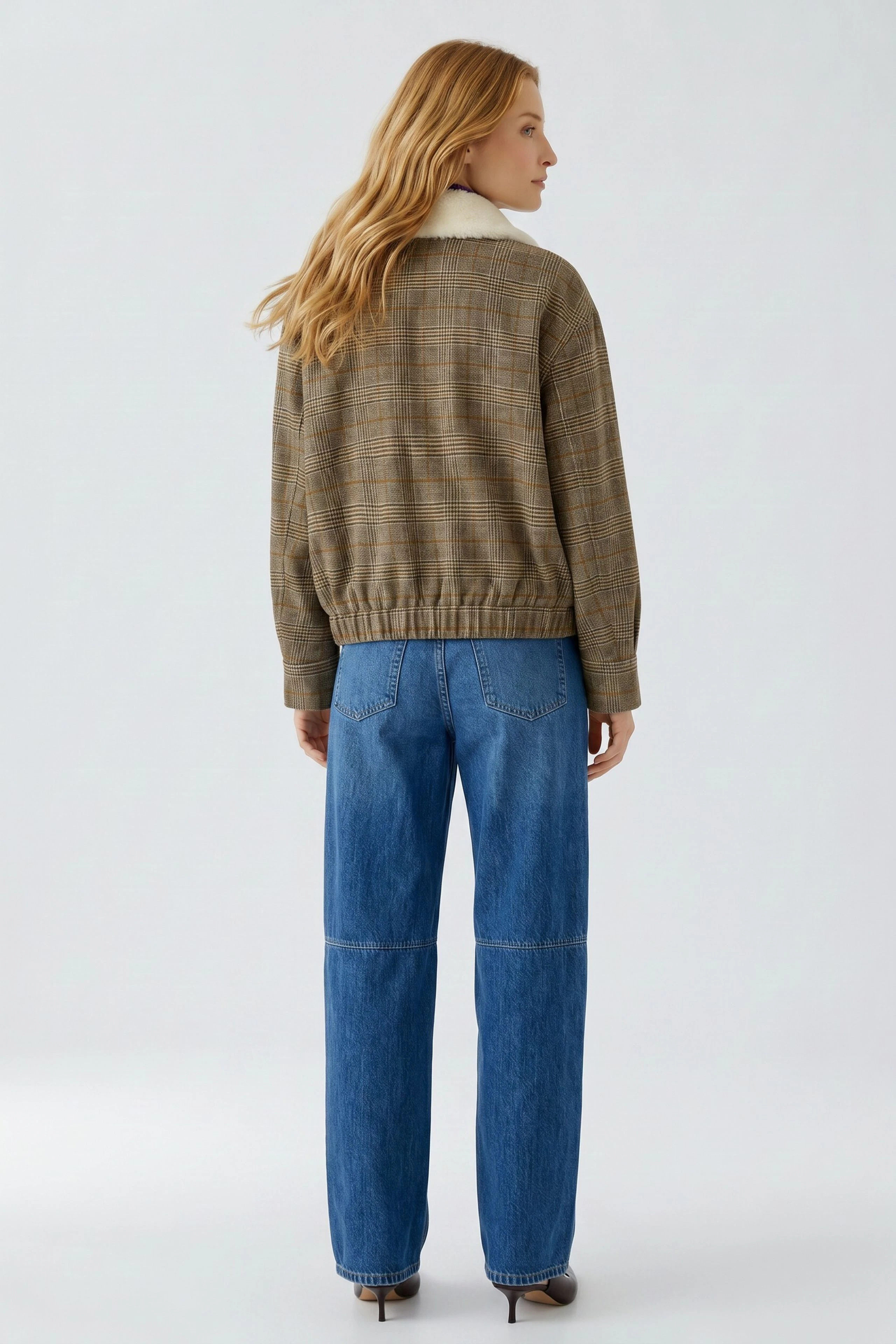 Casual blouson: Woman in a brown checkered blouson with a white collar, paired with blue jeans, facing away.
